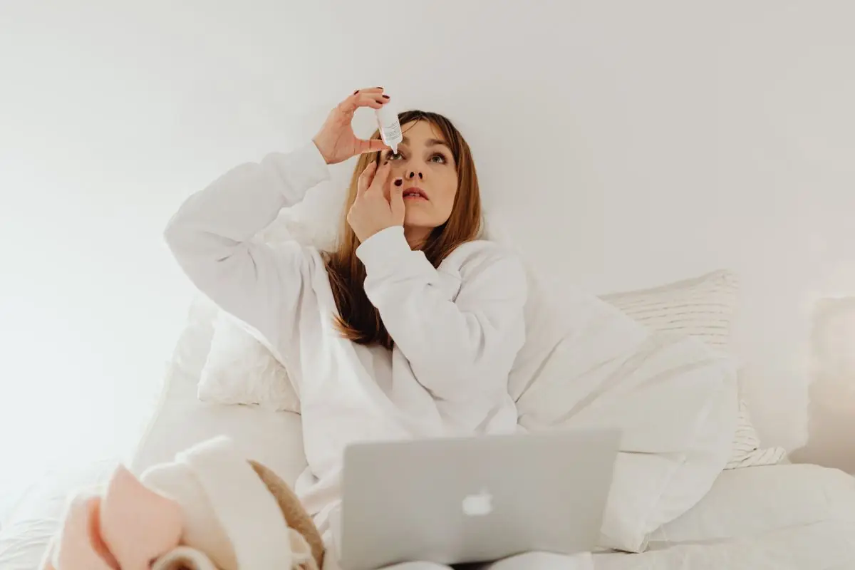 A woman putting a drop into her eye from a small bottle