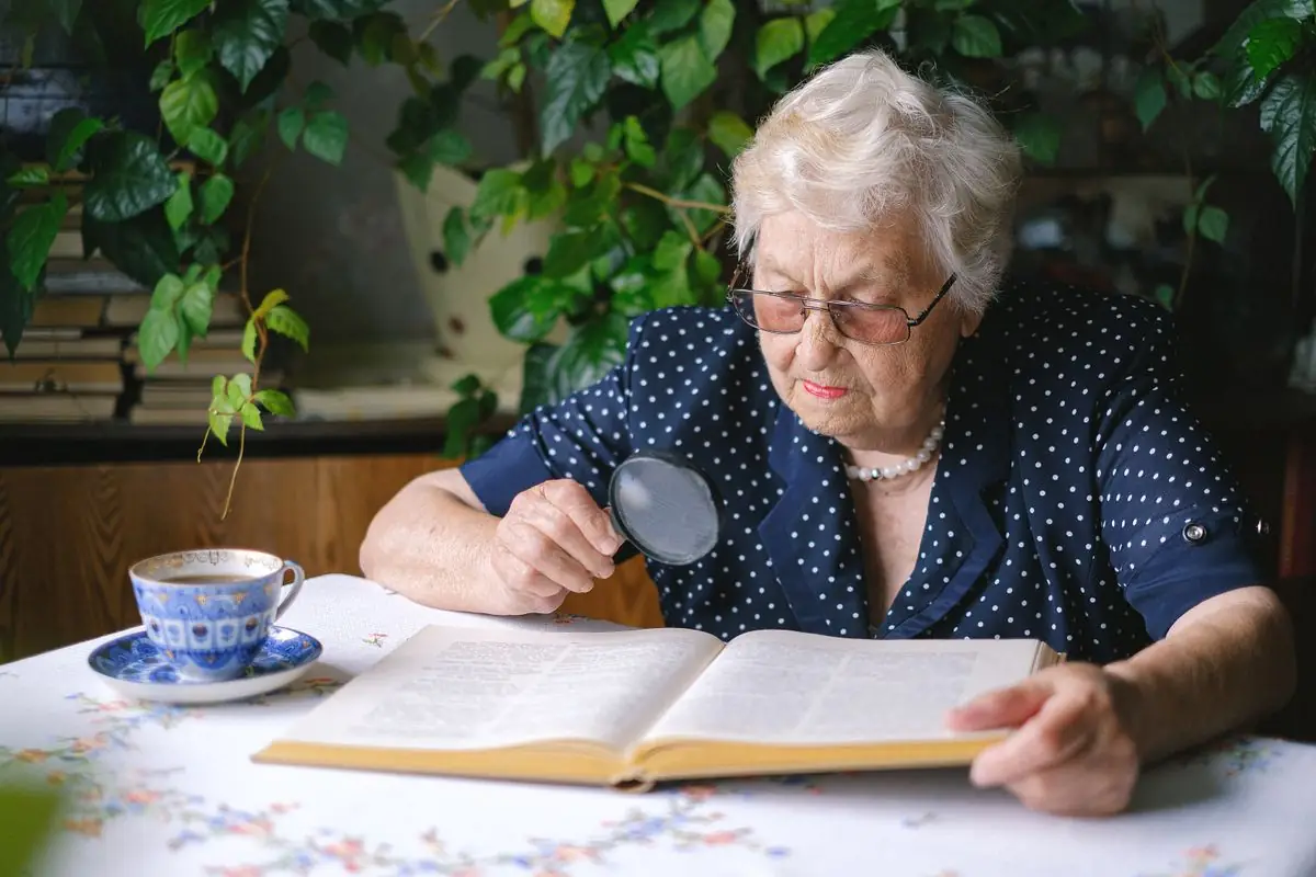 An older woman reading with a magnifier at a table